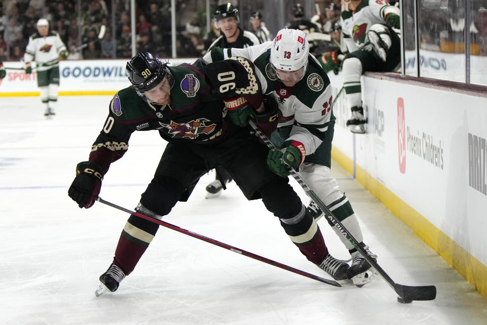 Arizona Coyotes defenseman J.J. Moser (90) and Minnesota Wild center Sam Steel battle for the puck in the second period during an NHL hockey game, Monday, Feb. 6, 2023, in Tempe, Ariz. (AP Photo/Rick Scuteri)