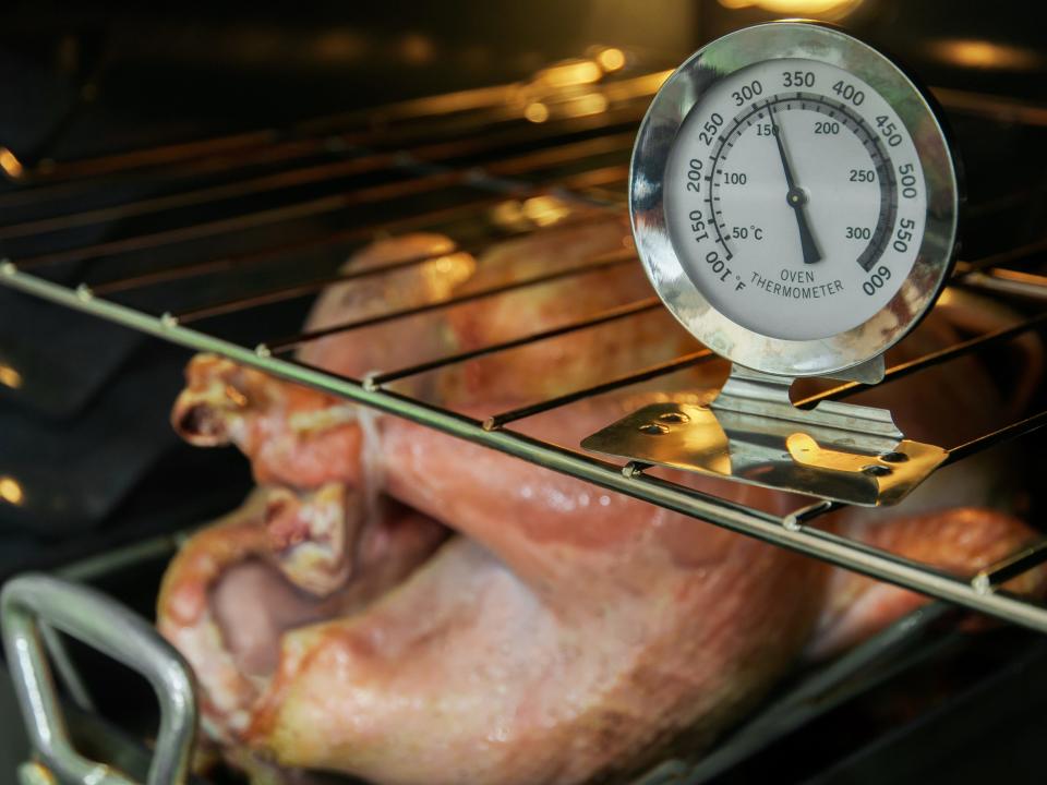 A thermometer in an oven next to a whole turkey baking