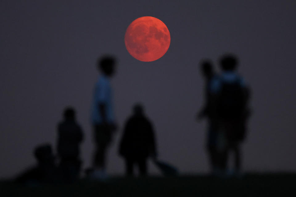 People watch the moon rise, with a red glow caused by smoke particles carried into the upper atmosphere from wildfires in North America, one day before a supermoon, on Parliament Hill in London, Britain, on August 18, 2024. / Copyright: Toby Melville/Reuters