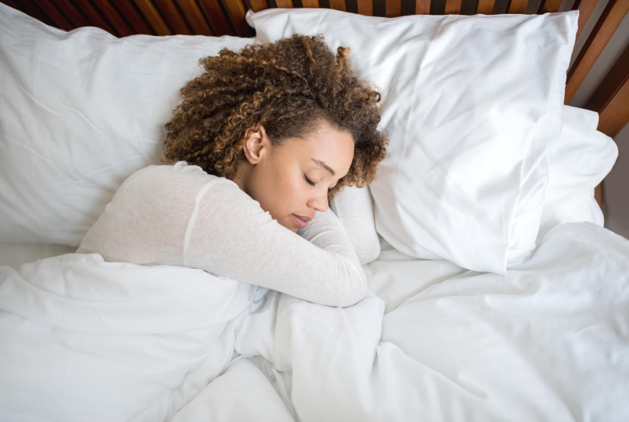 Tired African American woman sleeping in bed on mattress and pillows