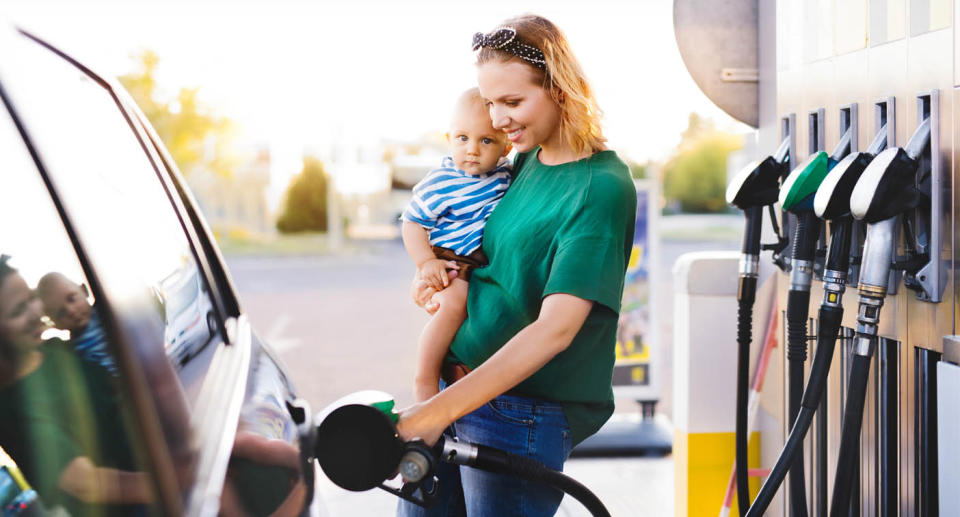 Woman filling up petrol while holding child on her hip. 