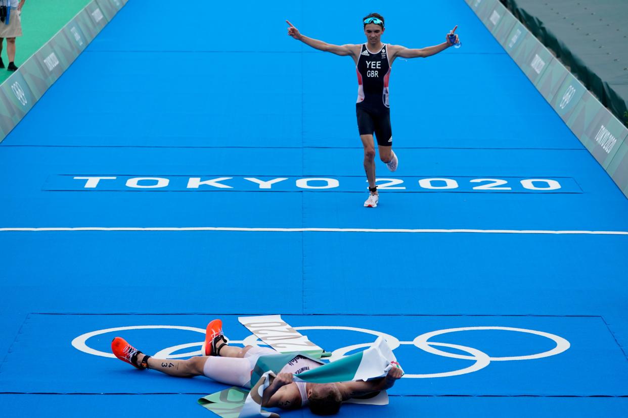 Kristian Blummenfelt of Norway celebrates his gold medal victory as Alex Yee of Great Britain crosses the finish line for the silver medal during the men's individual triathlon at the 2020 Summer Olympics, Monday, July 26, 2021, in Tokyo, Japan.