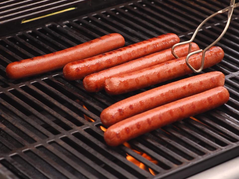 Hot dogs on grill being moved by tongs