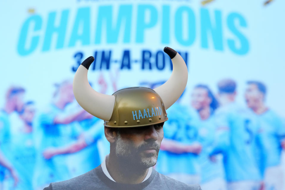 A cutout of Manchester City's head coach Pep Guardiola has a Viking helmet bearing the name of Erling Haaland placed on it by City supporters as they celebrate outside the Etihad stadium in Manchester, England, Saturday, May 20, 2023. Manchester City clinched the English Premier League title on Saturday after their nearest challengers Arsenal lost 1-0 to Nottingham Forest. (AP Photo/Jon Super)