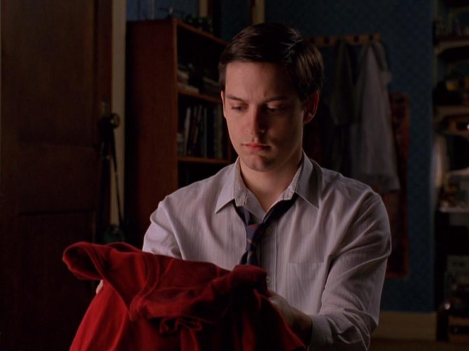 Peter Parker holding a red Spider-Man suit in his hands in "Spider-Man."