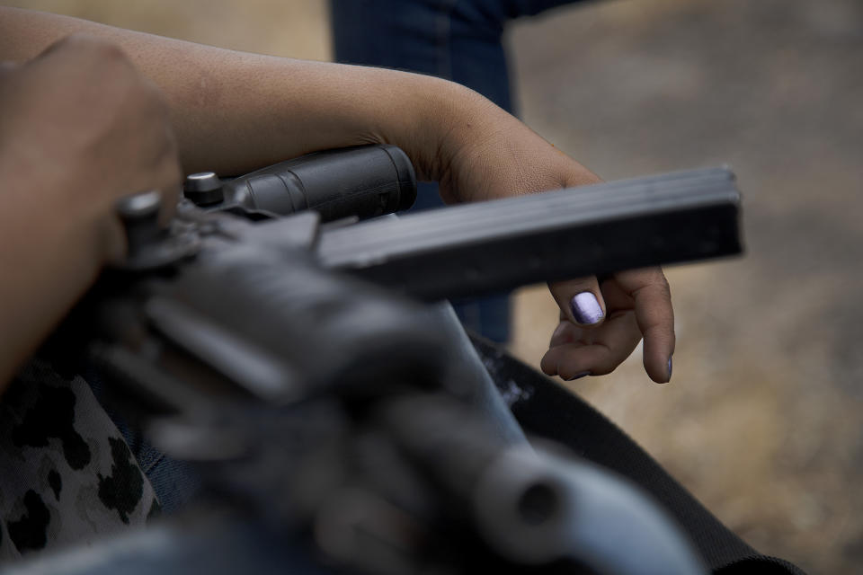 An armed woman who says she is a member of a female-led, self-defense group, sits guard at a checkpoint set up at the entrance of El Terrero in Michoacan state, Mexico, Thursday, Jan. 14, 2021. The vigilantes bitterly deny allegations they're part of a criminal gang, though they clearly see the Jalisco cartel as their foe. They say they would be more than happy for police and soldiers to come in and do their jobs. (AP Photo/Armando Solis)