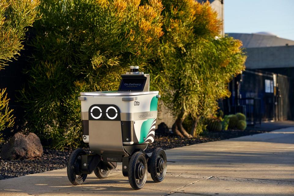 A four-wheeled delivery robot rolling along a sidewalk.