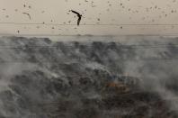 An excavator tries to contain the fire as smoke billows from burning garbage at the Ghazipur landfill site in New Delhi