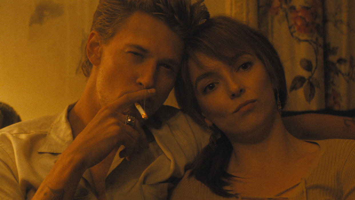  Austin Butler smokes a cigarette while sitting on a couch next to Jodie Comer in The Bikeriders. 