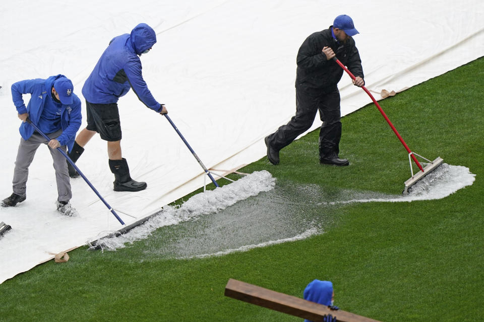 Groundskeepers remove water from a tarp as a baseball game between the New York Mets and the Atlanta Braves is postponed due to rain, Sunday, May 30, 2021, in New York. (AP Photo/Kathy Willens)