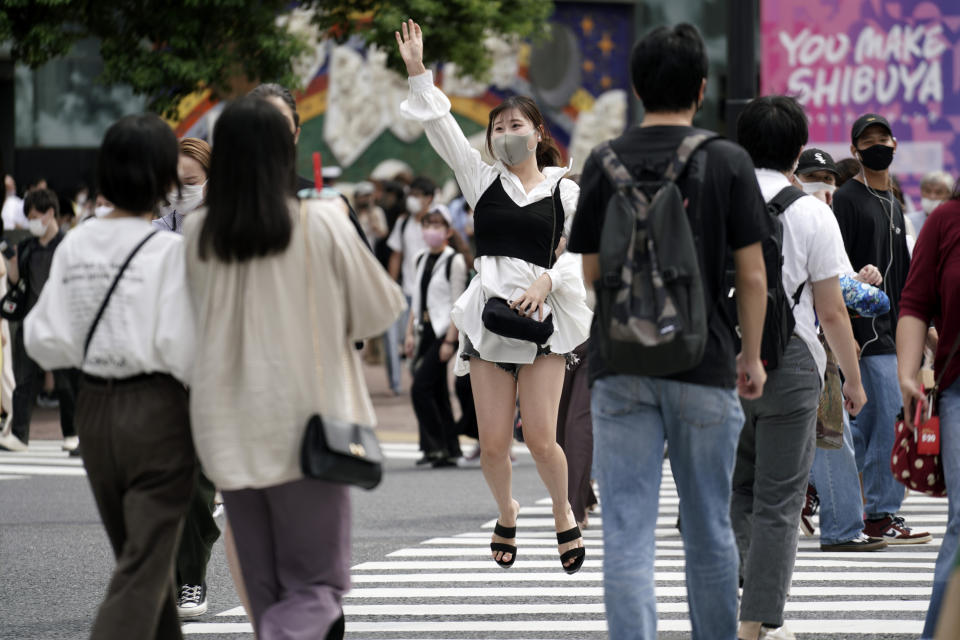 A woman wearing a protective mask to help curb the spread of the coronavirus jumps at Shibuya pedestrian crossings Monday, Sept. 21, 2020, in Tokyo. The Japanese capital confirmed more than 90 coronavirus cases on Monday marking Respect-for-the-Aged Day holiday. (AP Photo/Eugene Hoshiko)