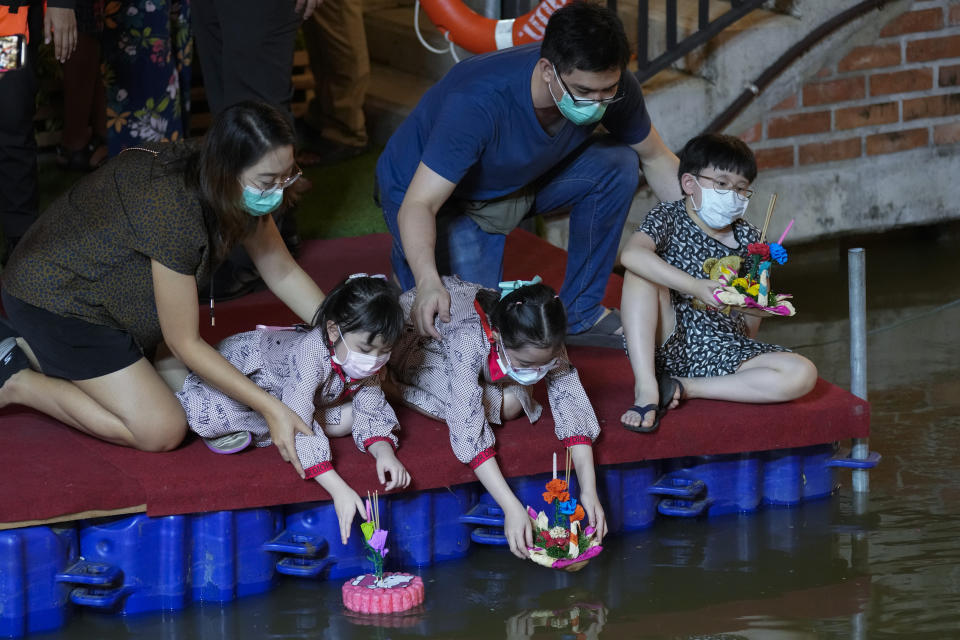 A Thai family places krathongs, small boats made of corn and decorated with banana leaves and flowers, into a Ong Ang canal during Loy Krathong festival in Bangkok, Thailand, Friday, Nov. 19, 2021. Thais believe that the candle-lit boats launched during the charming and popular Loy Krathong festival can carry the year's misfortunes away with them, but workers must clean up the waterways afterward to keep them from getting clogged and polluted. (AP Photo/Sakchai Lalit)