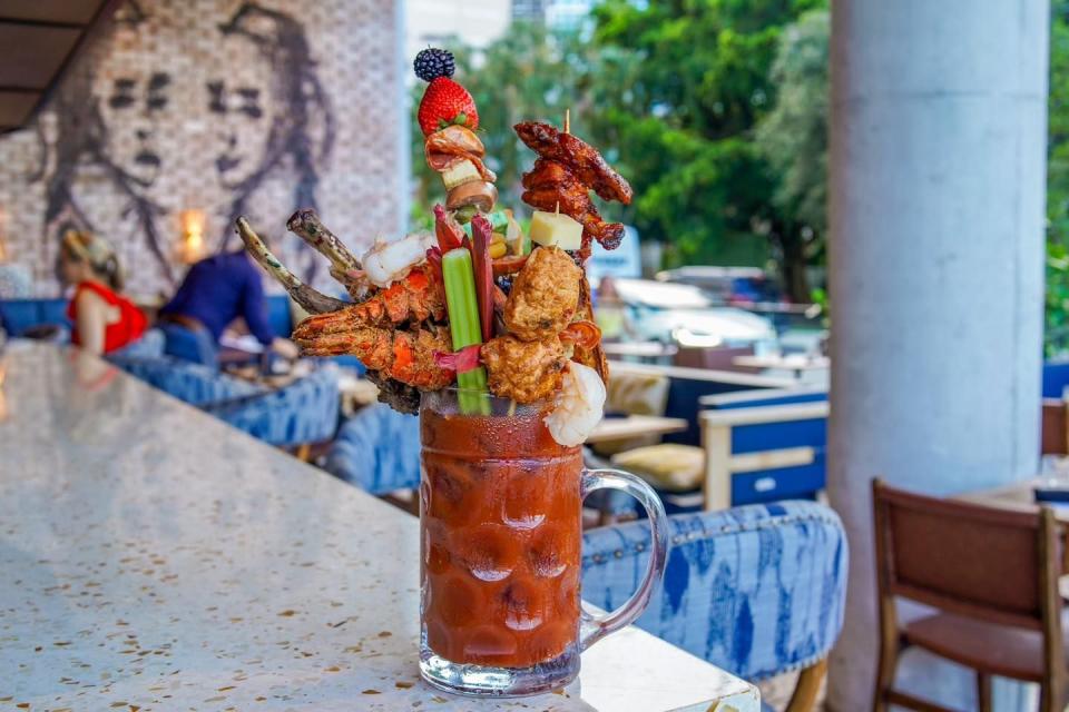 a clear glass with a bloody mary drink inside with toppings like chicken wings celery and lobster on top