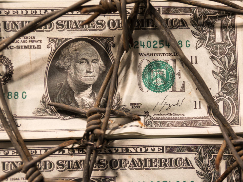 A U.S. $1 bill wrapped in barbed wire.