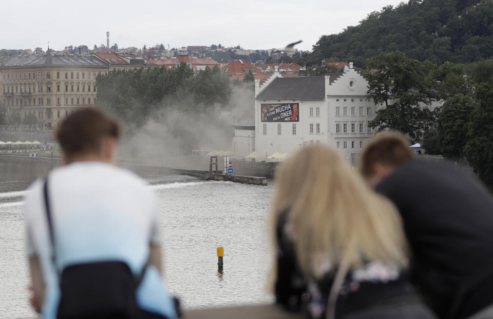 People watch as smoke rises from a technical building of the Kampa Museum in Prague, Czech Republic, Wednesday, July 15, 2020. It was immediately not clear if any of the art pieces were damaged. Kampa Museum is known for its valuable collections of paintings by Frantisek Kupka, a pioneer of modern abstract painting. (AP Photo/Petr David Josek)