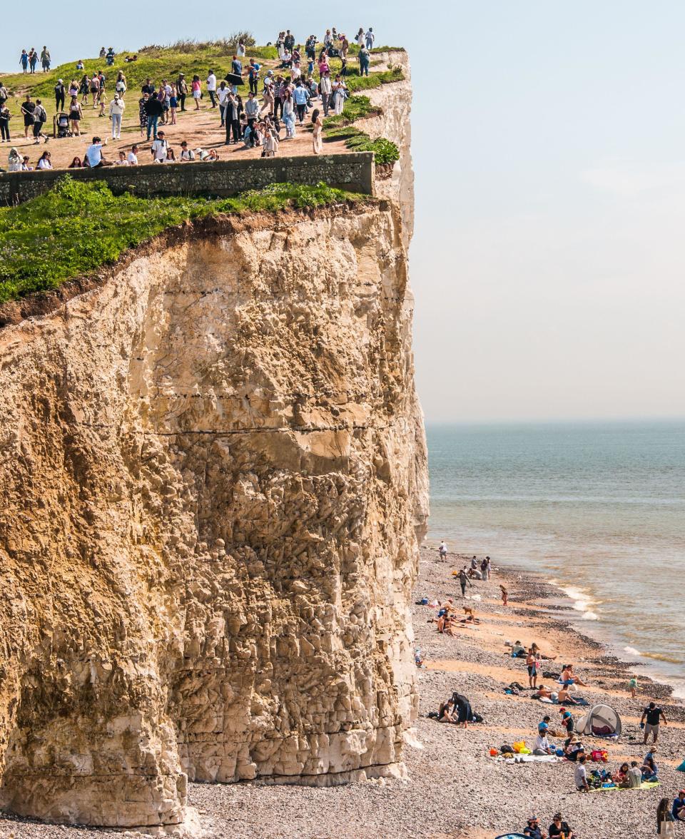 Birling Gap, Eastbourne, East Sussex, UK. 12th May 2024. The warmest day of the year thus far brings throngs of visitors to the picturesque National Trust site on the South coast. Many seem unaware of the risks they are taking on or very near to the crumbling undercut cliff edge. Danger signage seems most inadequte & there is no safety rope in this area. The rope from Beachy Head to Belle Tout lighthouse does not continue down to Birling Gap. The photographer regularly warns people to come back from the edge, most are appreciative & seem unaware of the danger. David Burr/Alamy Live News.