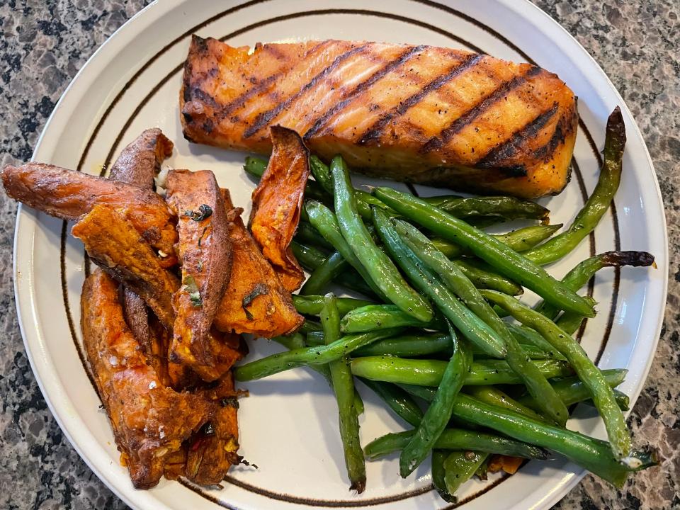 A plate with salmon with grill marks, sweet-potato wedges, and green beans