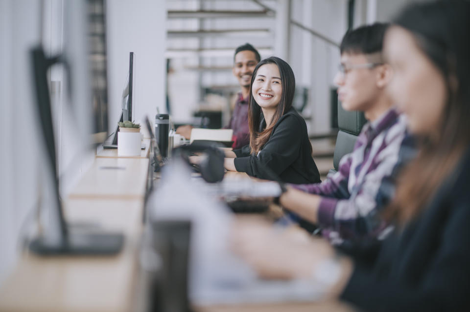 Asian Chinese woman smiling while talking to her colleagues at her workplace, illustrating a story on retrenchments in Singapore.