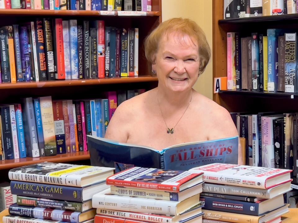 Linden Ponds librarian Suzanne Monk uses the tallest book she could find to provide coverage as part of the senior living community's 2024 fundraising calendar. Monk is Miss September.