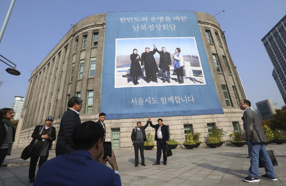 Two men pose in front of a banner showing a photo of South Korean President Moon Jae-in, second from right, his wife Kim Jung-sook, right, North Korean leader Kim Jong Un and Kim's wife Ri Sol Ju on North Korea's Mount Paektu, at Seoul City Hall in Seoul, South Korea, Tuesday, Oct. 23, 2018. The government of Moon formally approved the rapprochement deals he made with Kim last month. The signs read: "The summit between South and North Korea." (AP Photo/Ahn Young-joon)