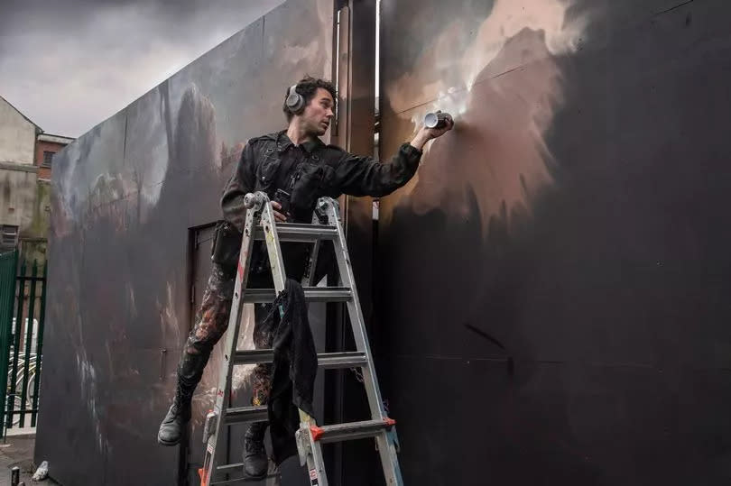 Belfast Street Art Festival with man in overalls spray painting wall in dark colours