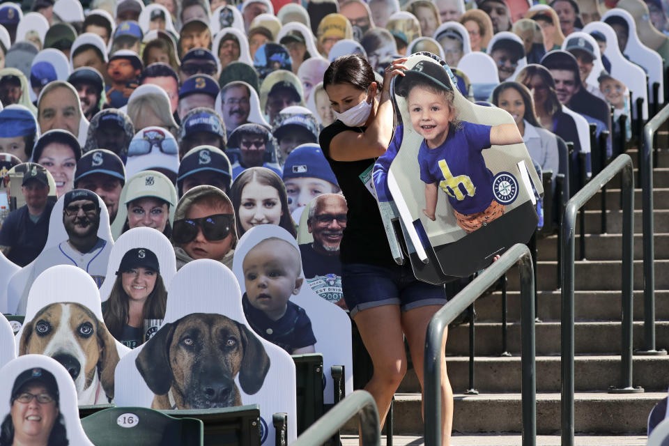 Seattle Mariners worker Lindsay Garza carries cutouts of fans to place in seats at the team's ballpark as part of the "Mariners Seat Fleet", Monday, July 27, 2020, in Seattle. The Mariners open play at home against the Oakland Athletics on Friday. For $30, fans can buy a version of themselves that will sit in at all home games. A portion of every purchase will be donated to non-profit organizations supporting COVID-19-related relief efforts. If a cutout "catches" a foul ball during a game, the team will mail the fan the baseball. (AP Photo/Elaine Thompson)