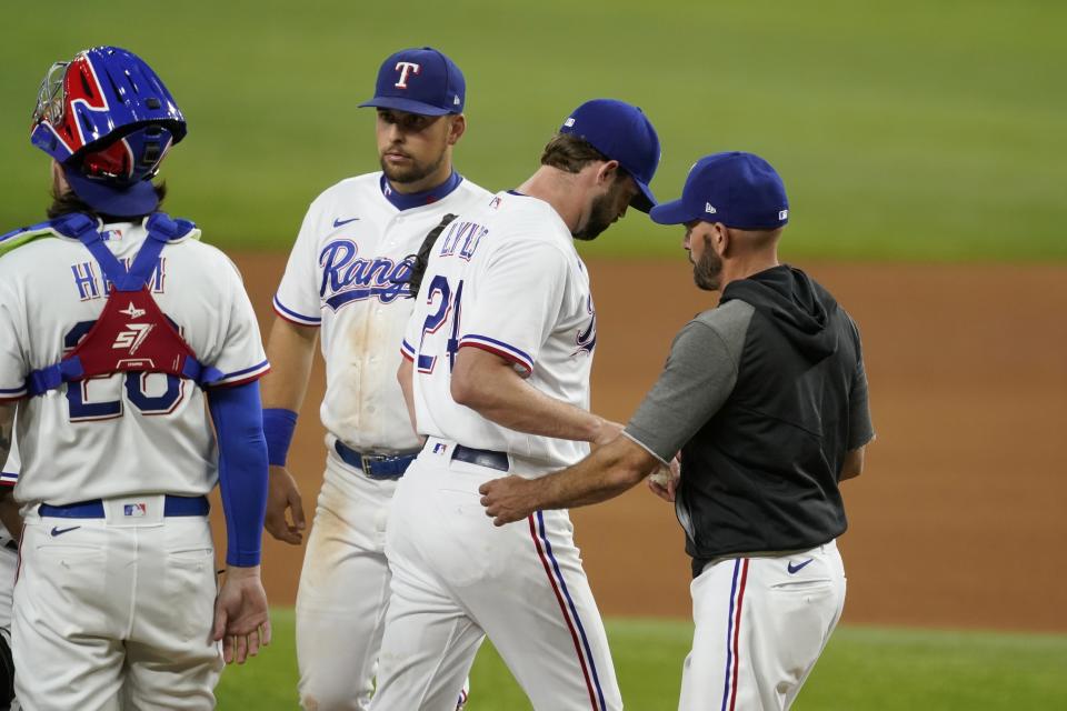 Texas Rangers catcher Jonah Heim, left, and Nathaniel Lowe, second from left, stand on the mound as starting pitcher Jordan Lyles (24) turns the ball over to manager Chris Woodward, right, in the seventh inning of a baseball game in Arlington, Texas, Saturday, Aug. 14, 2021. (AP Photo/Tony Gutierrez)
