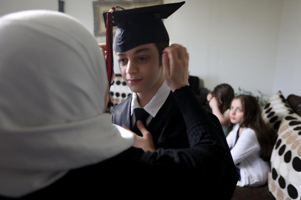 Hanan Marza helps her son, Adam Ismail with his cap and  gown before eighth grade graduation. Shaimaa Ismail is shown in the background. Tuesday, June 22, 2021