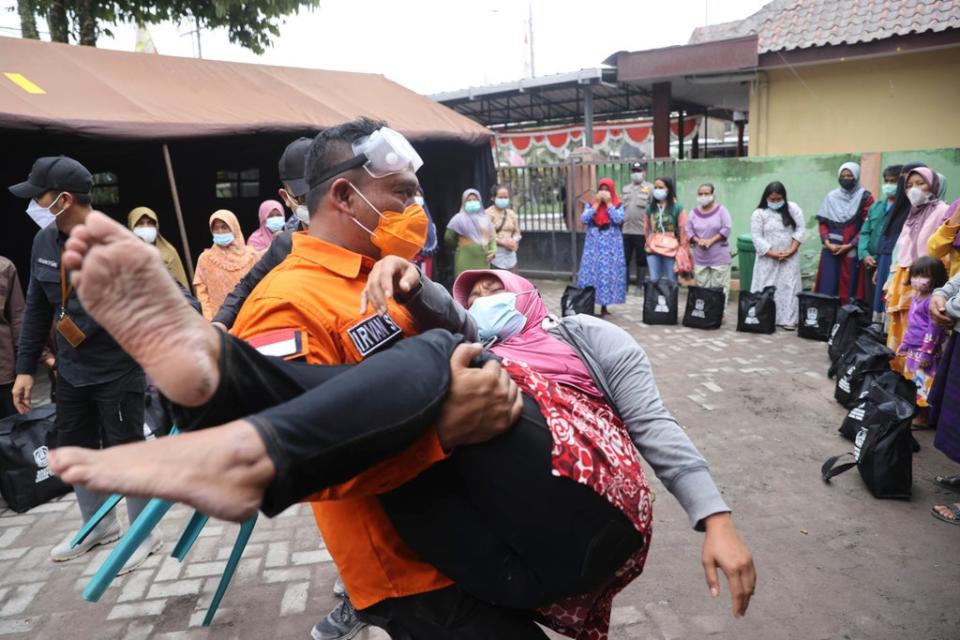 A rescuer carries a woman who fainted after the eruption of Mount Semeru (AP)