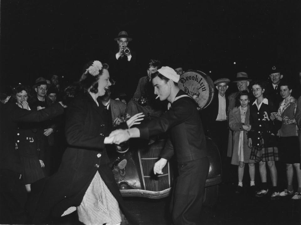 <p>A sailor dances with a laughing women in Times Square as a brass band strikes up a tune on the hood of a car.</p>