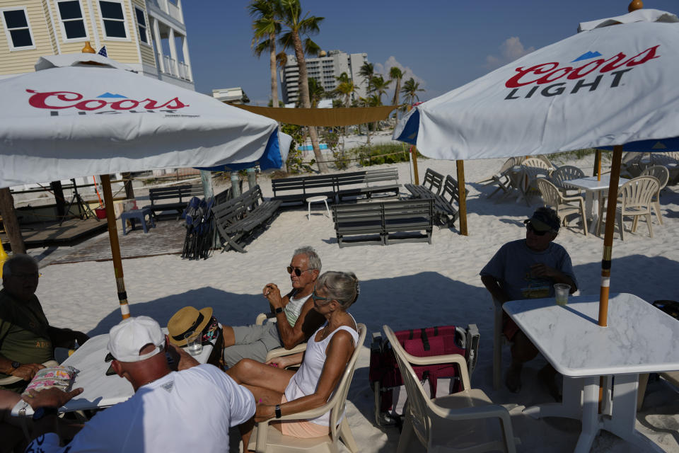 A mix of local residents and visitors sit outside at The Beach Bar, which was one of the early businesses to reopen out of a trailer last January, several months after Hurricane Ian, in Fort Myers Beach, Fla., Wednesday, May 10, 2023. The bar's ownership hopes to start rebuilding their bar and two apartments this summer, this time out of concrete instead of wood. (AP Photo/Rebecca Blackwell)