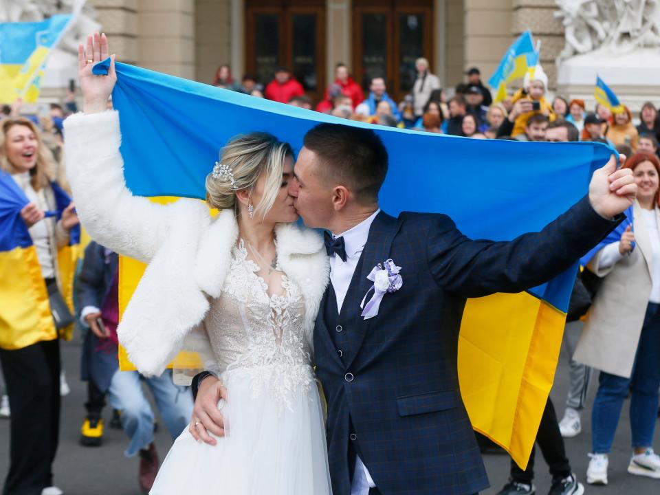 Newly wed Ukrainians hold a Ukrainian flag and kiss as Kherson residents temporarily living in Odesa celebrate the liberation of their native town in Odesa on 12 November 2022, amid Russia's invasion of Ukraine.