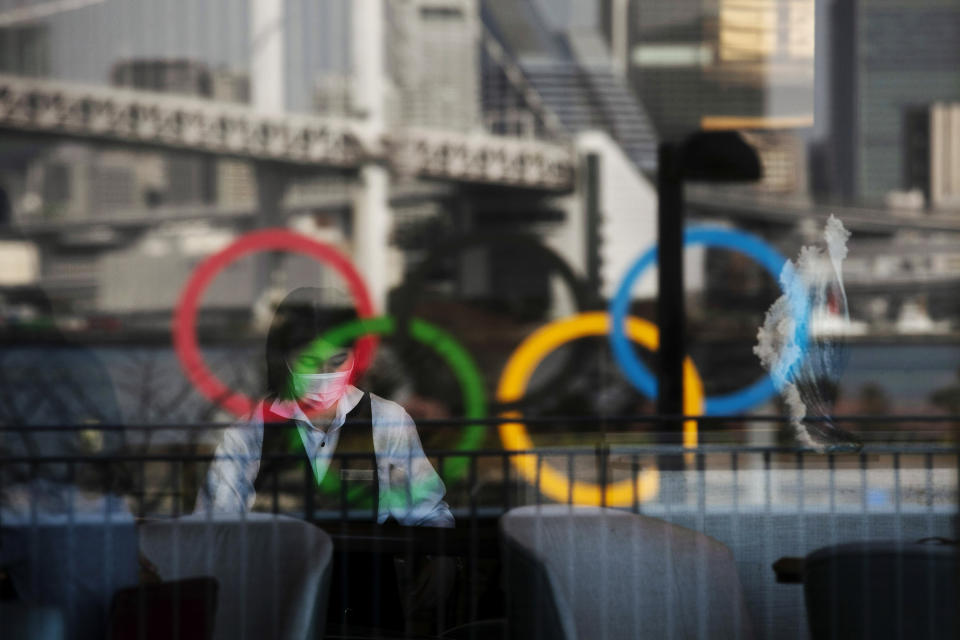 FILE - In this Feb. 24, 2020, photo, the Olympics rings are reflected on the window of a hotel restaurant as a server with a mask sets up a table, in the Odaiba section of Tokyo. Japan on Friday, April 23, declared a state of emergency to curb a rapid coronavirus resurgence, the third since the pandemic began. The measures in parts of Japan, including Tokyo, have so far failed to curb infections caused by a more contagious new variant of the virus. (AP Photo/Jae C. Hong, File)