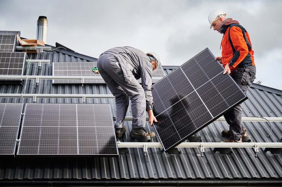Two workers install solar panels on a roof.