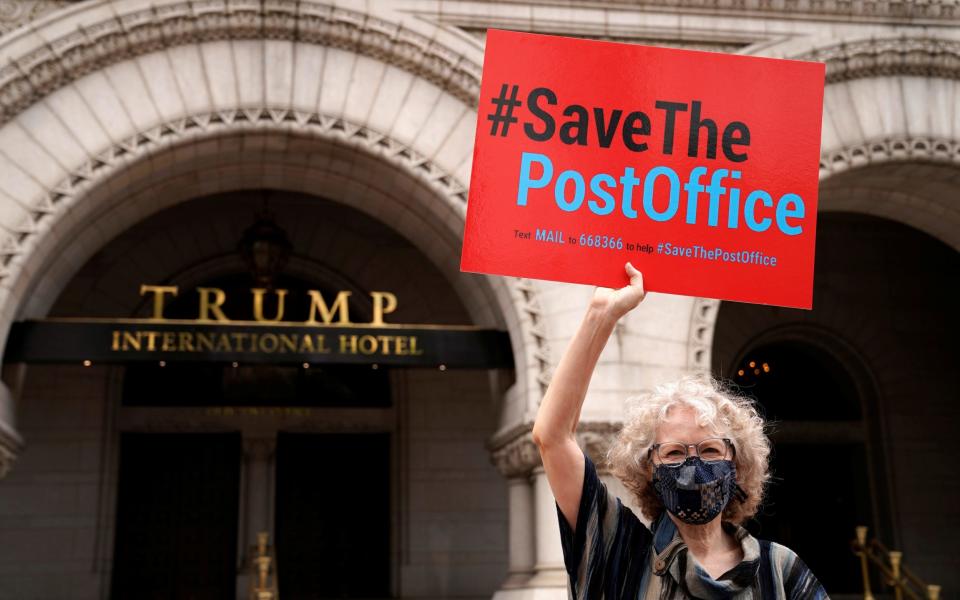 A protester holds up a sign in support of the US Postal Service outside the Trump Hotel in Washington DC - Erin Scott/Reuters