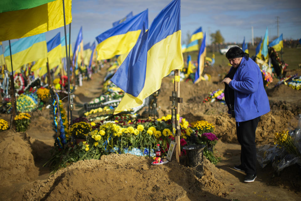 Lyubov Mamedova, the mother of a recently killed Ukrainian serviceman Ruslan Mamedov, stands next to his grave in a cemetery during Ukraine Defenders Day in Kharkiv, Ukraine, Friday, Oct. 14, 2022. (AP Photo/Francisco Seco)
