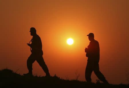 Border Security Force (BSF) soldiers patrol as they are silhouetted against the setting sun at the fenced border with Pakistan at Babiya village in Hira Nagar sector, about 80 km (50 miles) from Jammu December 6, 2013. REUTERS/Mukesh Gupta/Files