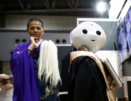 A Buddhist monk looks at a 'robot priest' wearing a Buddhist robe during its demonstration at Life Ending Industry EXPO 2017 in Tokyo, Japan August 23, 2017. REUTERS/Kim Kyung-Hoon