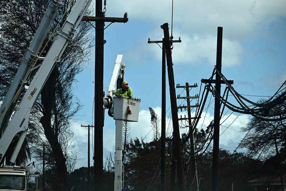 <p> PATRICK T. FALLON/AFP via Getty Images</p> Electricians work on power lines in the aftermath of the Maui wildfires in Lahaina, Hawaii.