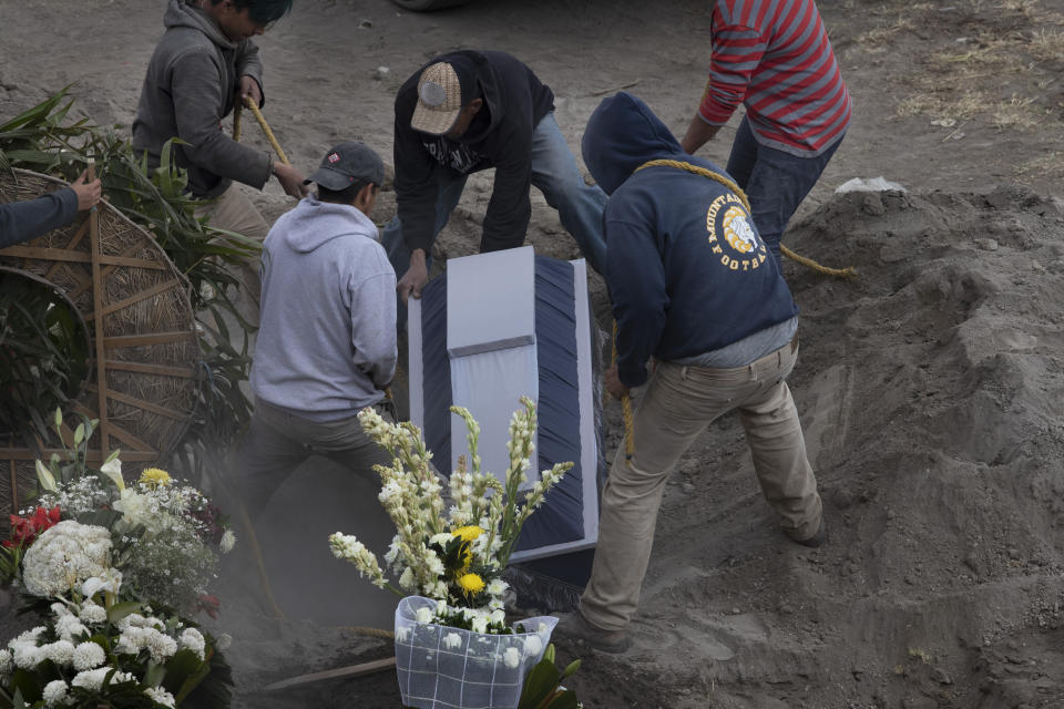 Workers place the coffin of 86-year-old Gabina Salgado Husca, who died of complications related to the new coronavirus, into her grave in the Valle de Chalco municipal cemetery on the outskirts of Mexico City, Wednesday, Nov. 18, 2020. (AP Photo/Marco Ugarte)