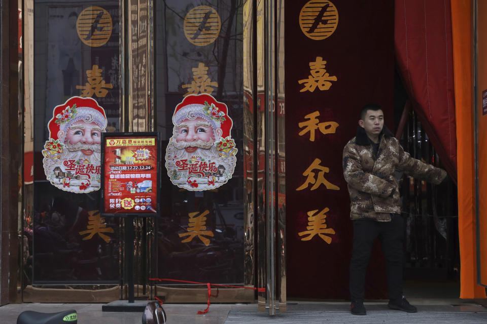 In this Saturday, Dec. 22, 2018, photo, a worker guards the entrance of a shop decorated with images of Santa Claus in Zhangjiakou in northern China's Hebei province. At least four Chinese cities and one county have restricted Christmas celebrations this year. Churches in another city have been warned to keep minors away from Christmas, and at least ten schools nationwide have curtailed Christmas on campus, The Associated Press has found. (AP Photo/Ng Han Guan)