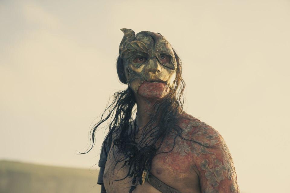 A masked and sunburnt man stares at a sunrise on the beach