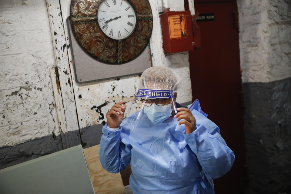 In this Thursday, April 23, 2020 photo, Ruth Caballero, a nurse with The Visiting Nurse Service of New York, suits up in protective equipment before treating a COVID-19 patient on her rounds in upper Manhattan in New York. Home care nurses, aides and attendants, who normally help an estimated 12 million Americans with everything from bathing to IV medications, are now taking on the difficult and potentially dangerous task of caring for coronavirus patients. (AP Photo/John Minchillo)