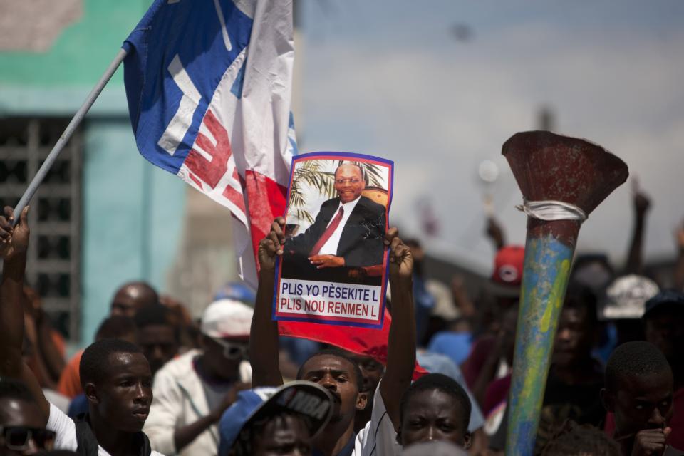 A demonstrator holds up a picture of Haiti's former President Jean-Bertrand Aristide, that reads in Creole "The more they persecute him, the more we love him", during a rally to mark the tenth anniversary of his second ouster in Port-au-Prince, Haiti, Thursday Feb. 27, 2014. The protesters denounced what they described as widespread corruption in the government of President Michel Martelly and even called for his resignation. (AP Photo/Dieu Nalio Chery)