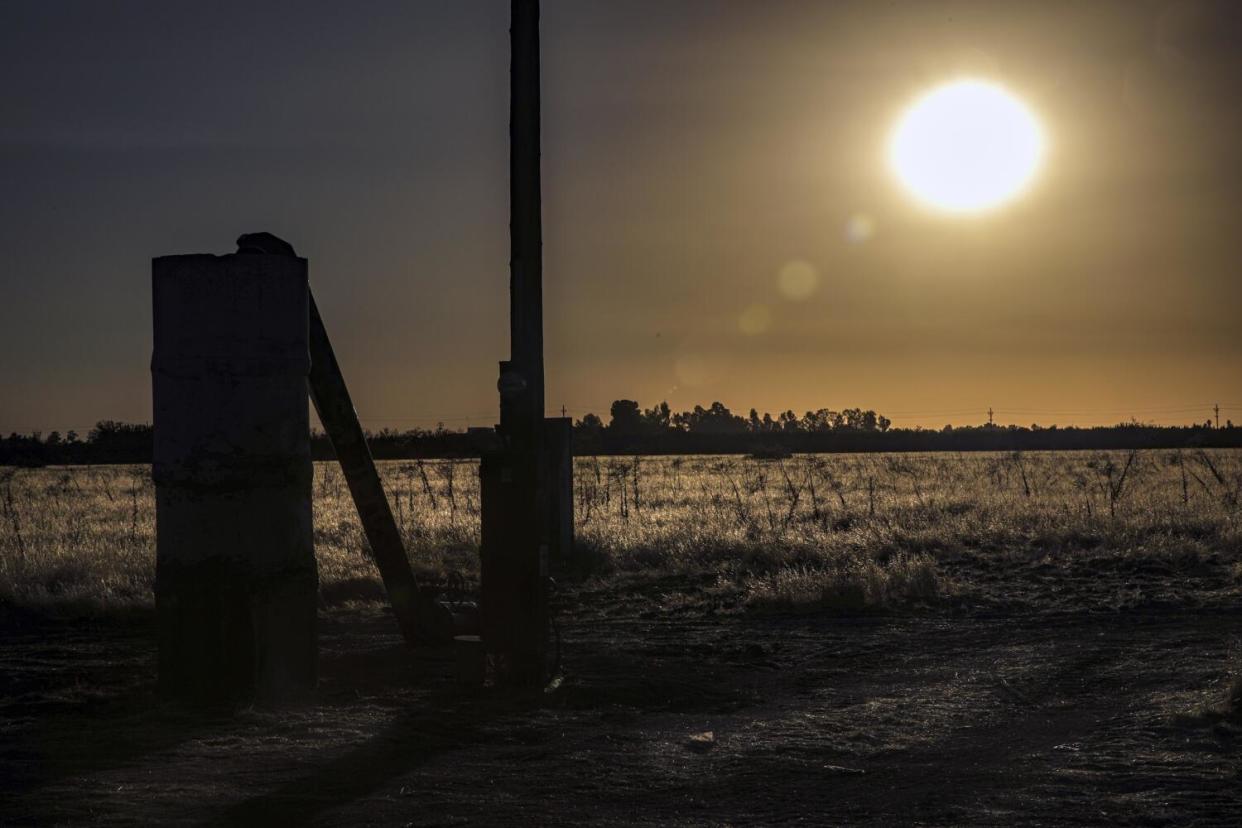 The standpipe and pump of an agricultural well are silhouetted at sunset near the community of Sultana.