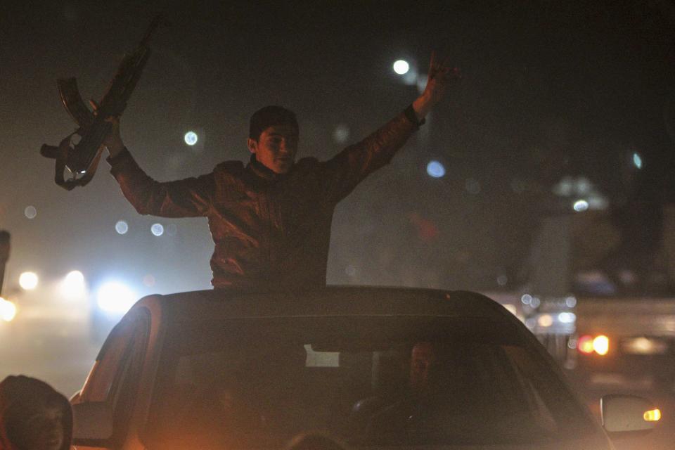 A Kurdish man holds up a weapon as he tours with others the streets of Ras al-Ain