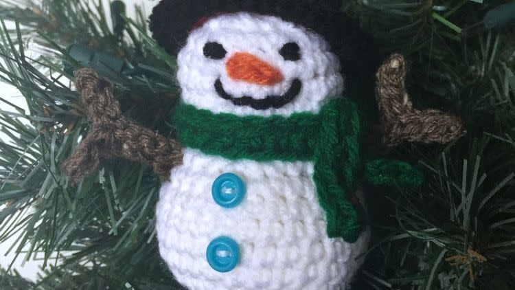 crochet smiling snowman ornament with two blue buttons on the belly