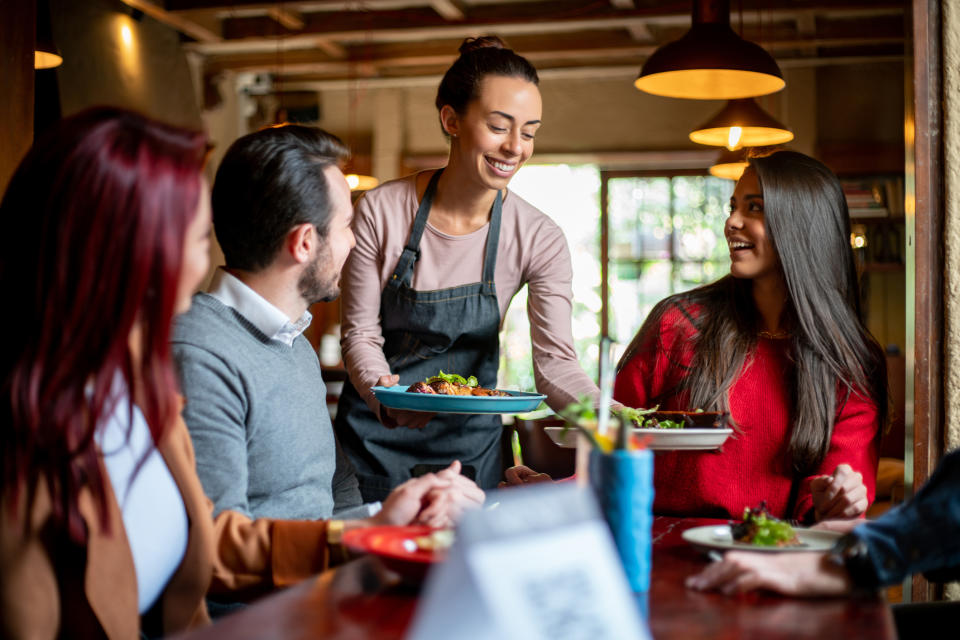 Waitress serving food to three smiling people at a restaurant table