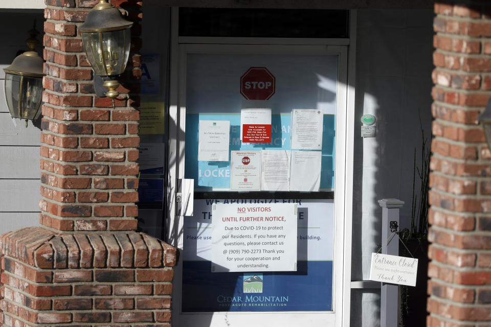 Warning notices are posted on a door at an entrance to the Cedar Mountain Post Acute nursing facility in Yucaipa, Calif., Wednesday, April 1, 2020. The Southern California nursing home has been hit hard by the coronavirus, with more than 50 residents infected, a troubling development amid cautious optimism that cases in the state may peak more slowly than expected. (AP Photo/Chris Carlson)