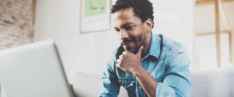 Smiling young African man making video call with friends while sitting on sofa at his modern home.Concept of happy business people.Blurred background, flare effect